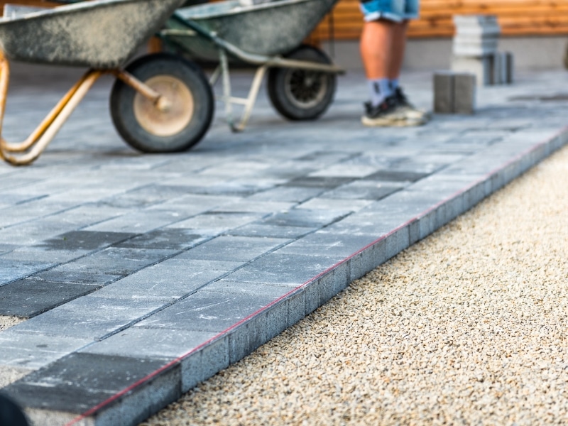 Patio paving installation with grey concrete blocks and gravel base.