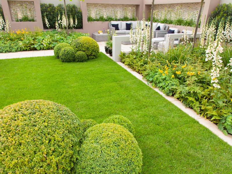 Outdoor landscaping with trimmed hedges, green lawn, and modern seating area