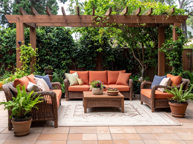 Cosy outdoor lounge under a wooden pergola surrounded by greenery, reflecting relaxed Australian cottage garden ideas.