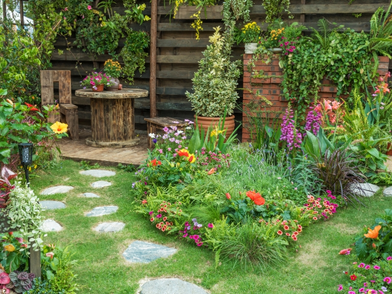 Rustic backyard with a stone path, wooden furniture, and colourful flowers showcasing charming cottage garden ideas.
